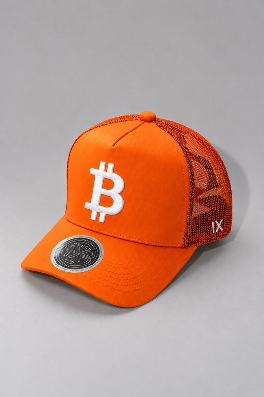 Angled view of MERCH IX orange Bitcoin trucker hat featuring raised white Bitcoin embroidery, orange mesh back panels, white IX side branding, curved brim, and metallic silver visor sticker.