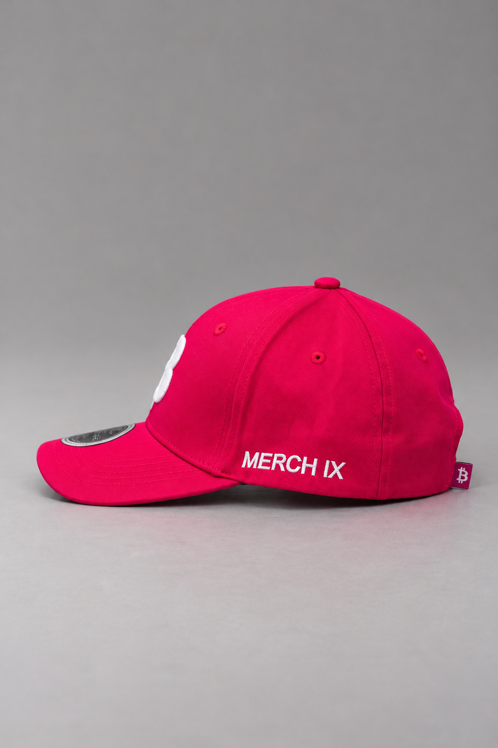Side profile of hot pink Bitcoin baseball cap featuring white MERCH IX embroidery, a curved brim, and a small Bitcoin woven tag at the rear.