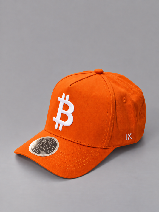 Angled view of orange MERCH IX Bitcoin cap showing raised white Bitcoin logo, white IX side embroidery, and metallic visor sticker.